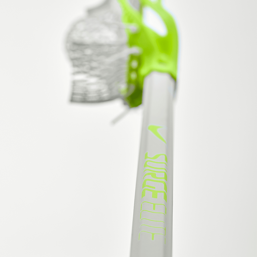 Close-up of a lacrosse stick highlighting the "SurgeLite" branding on the Nike Surge Elite Composite LE Lacrosse Shaft by Nike, featuring a green grip and mesh netting. The lightweight, durable shaft is prominently displayed against a plain white background, accentuating its Limited Edition Volt appeal.